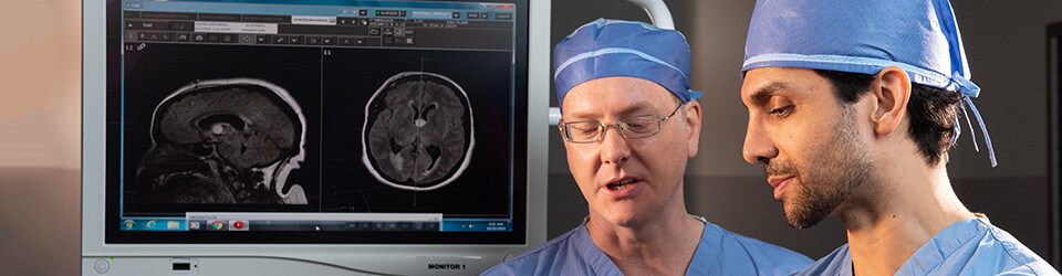 A pair of surgeons stand in the foreground of a scan on a screen
